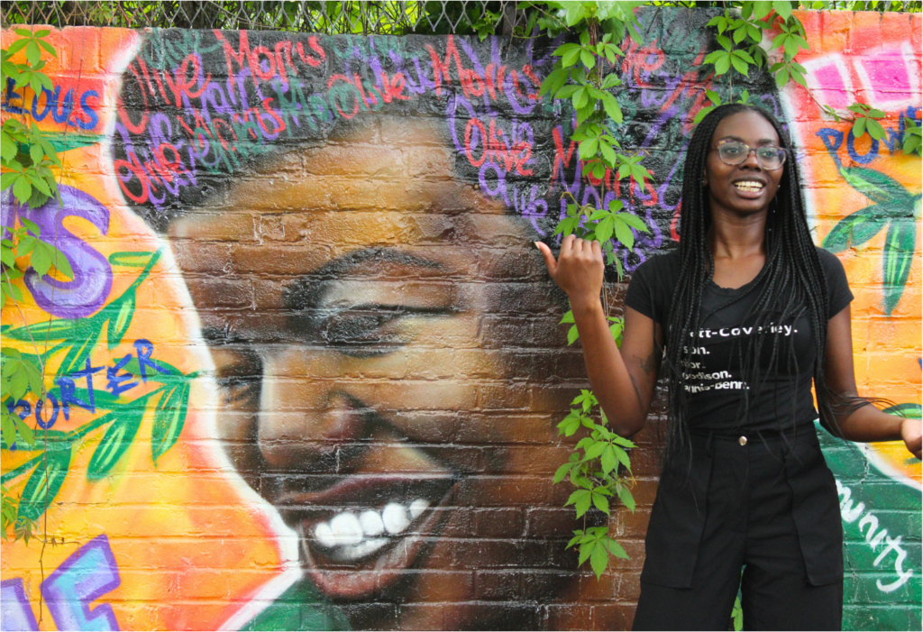 Jemmar pointing at a mural of Olive Morris, one of the UK's greatest community leaders and activists in the feminist, black nationalist and squatters rights campaigns of the 70's.