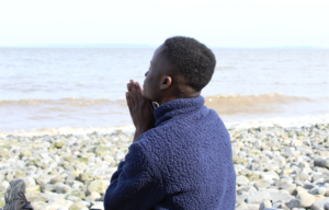 Adjei on a rocky beach with his hands together