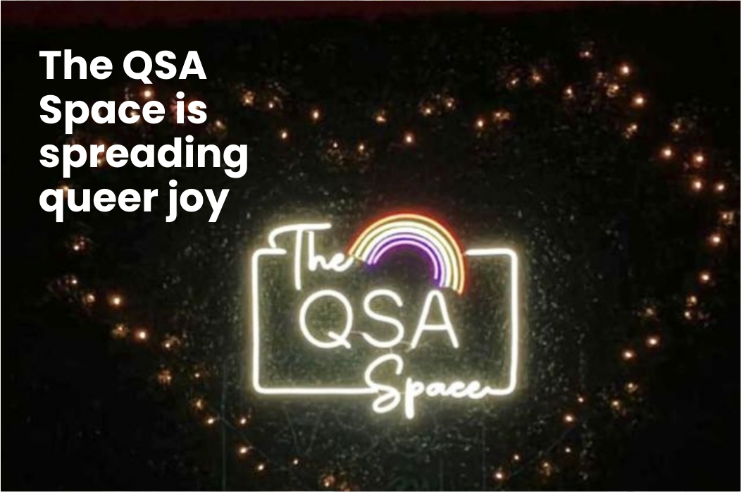 A neon sign with a rainbow and text - the QSA Space. Text on image - The QSA Space is spreading queer joy.