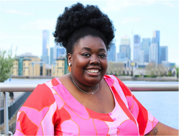 Shania-Sophia Dunbar Ives smiling at the camera in front of a city skyline.