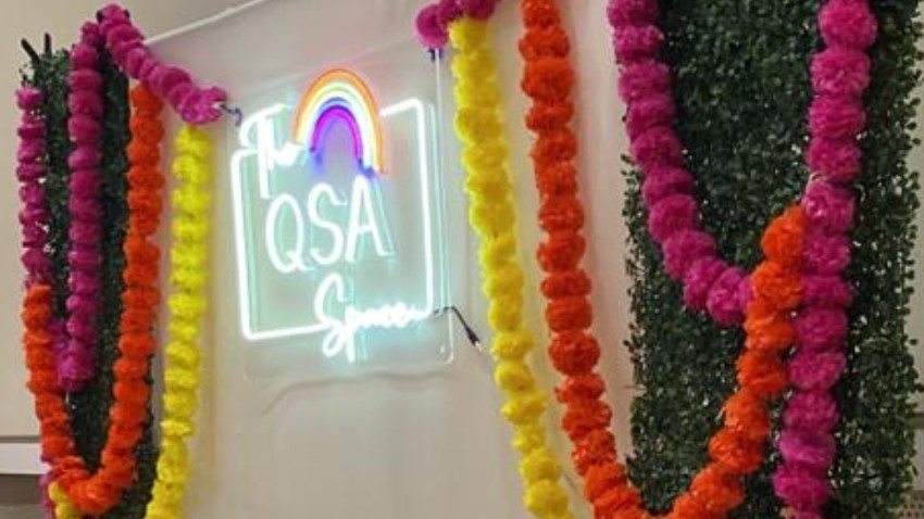 A white wall with colorful boarder and neon sign - The QSA Space.