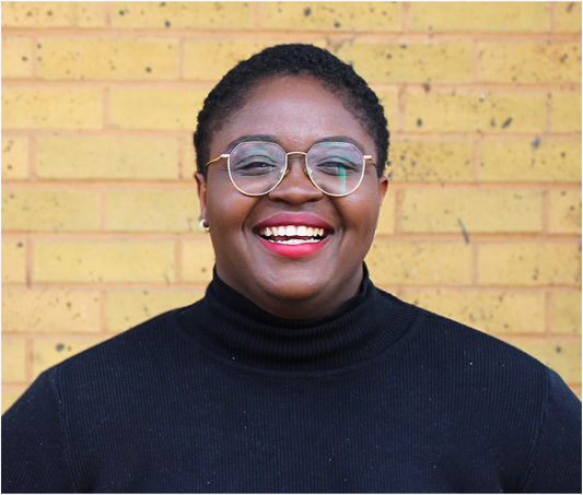 Fola Afolabi smiling in front of a brick wall