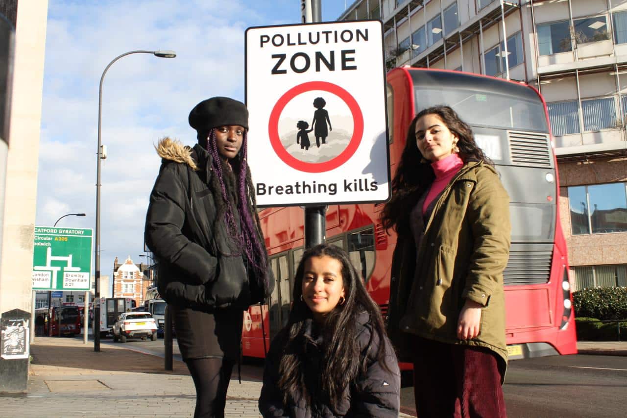 Three people standing by a 'pollution zone' sign 